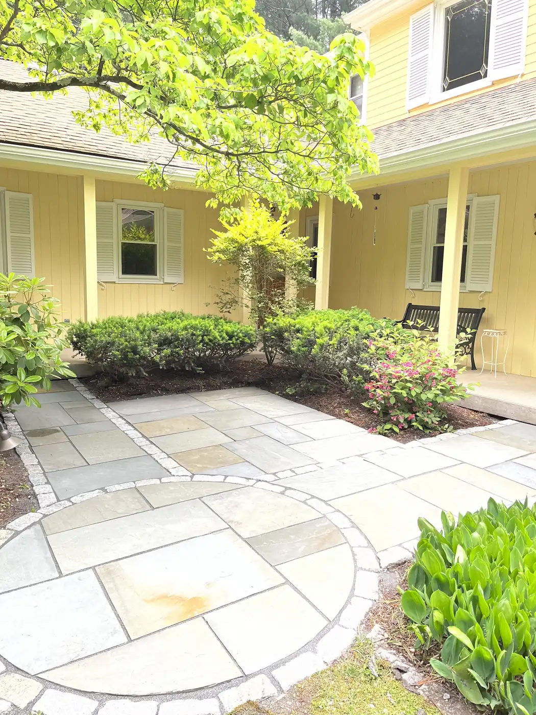 Bluestone courtyard with a circular cobble-edged inlay at a yellow home in Avon, CT