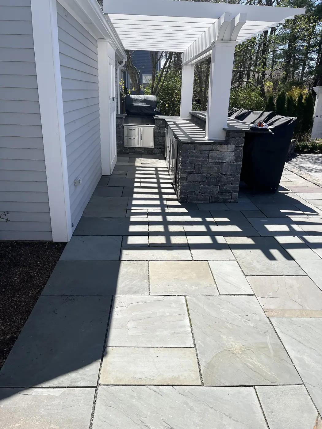 Bluestone patio with a stone outdoor kitchen under a white pergola in West Hartford, CT
