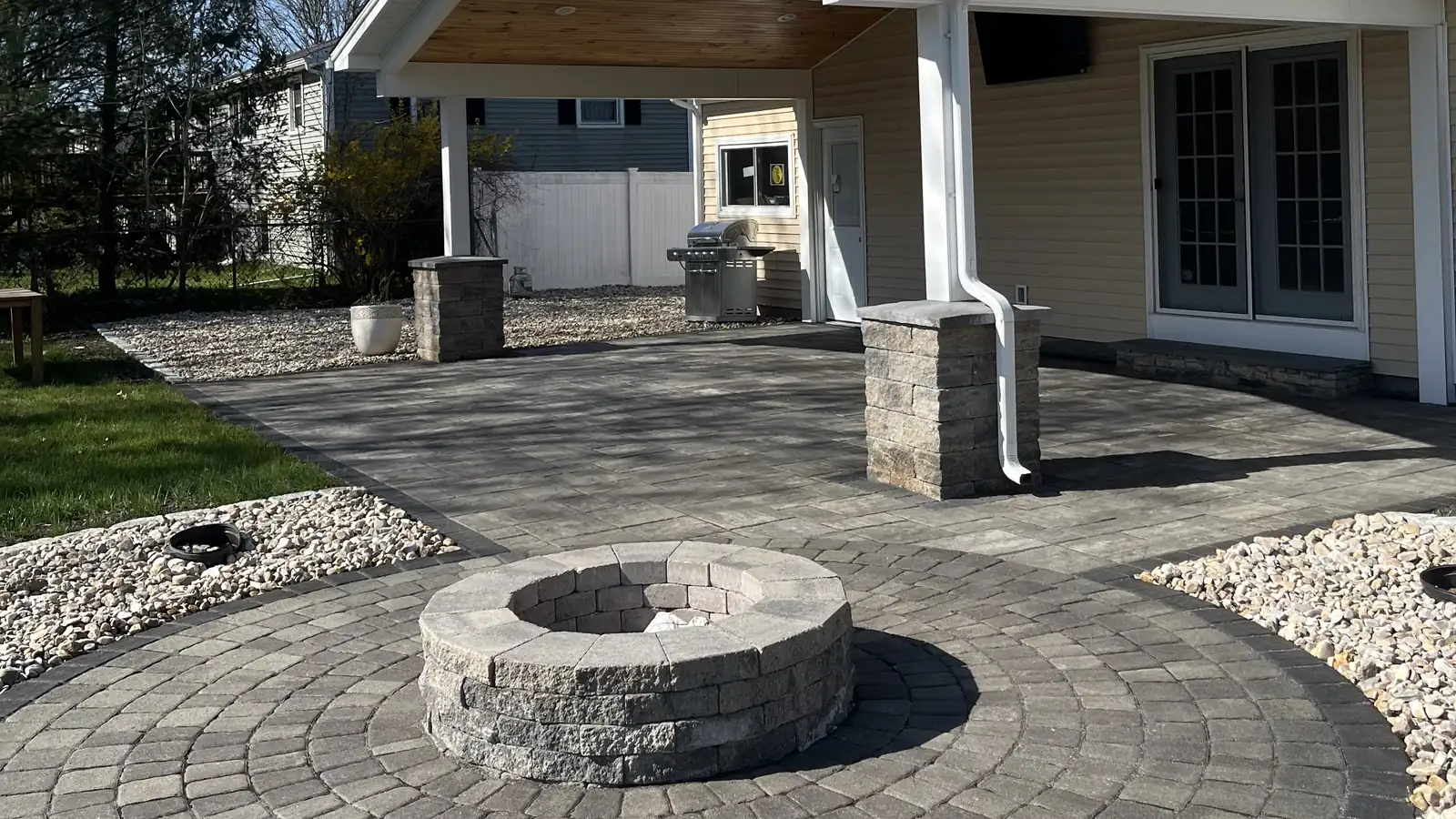 Circular paver fire pit patio with stone pillars near a covered porch in Southington, CT