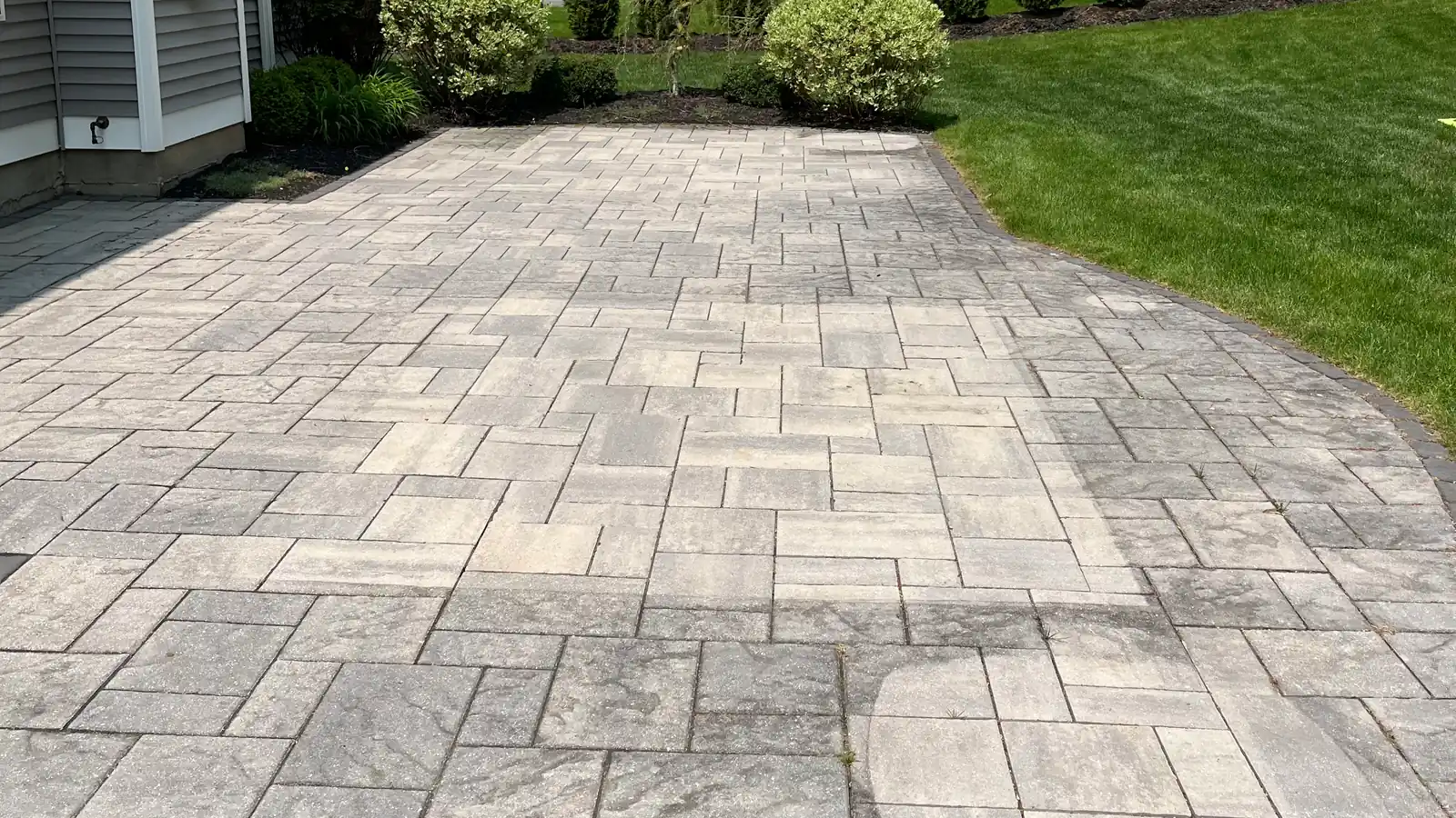 Freshly cleaned gray paver patio with a charcoal border and arborvitae hedge behind a home in Southington, CT