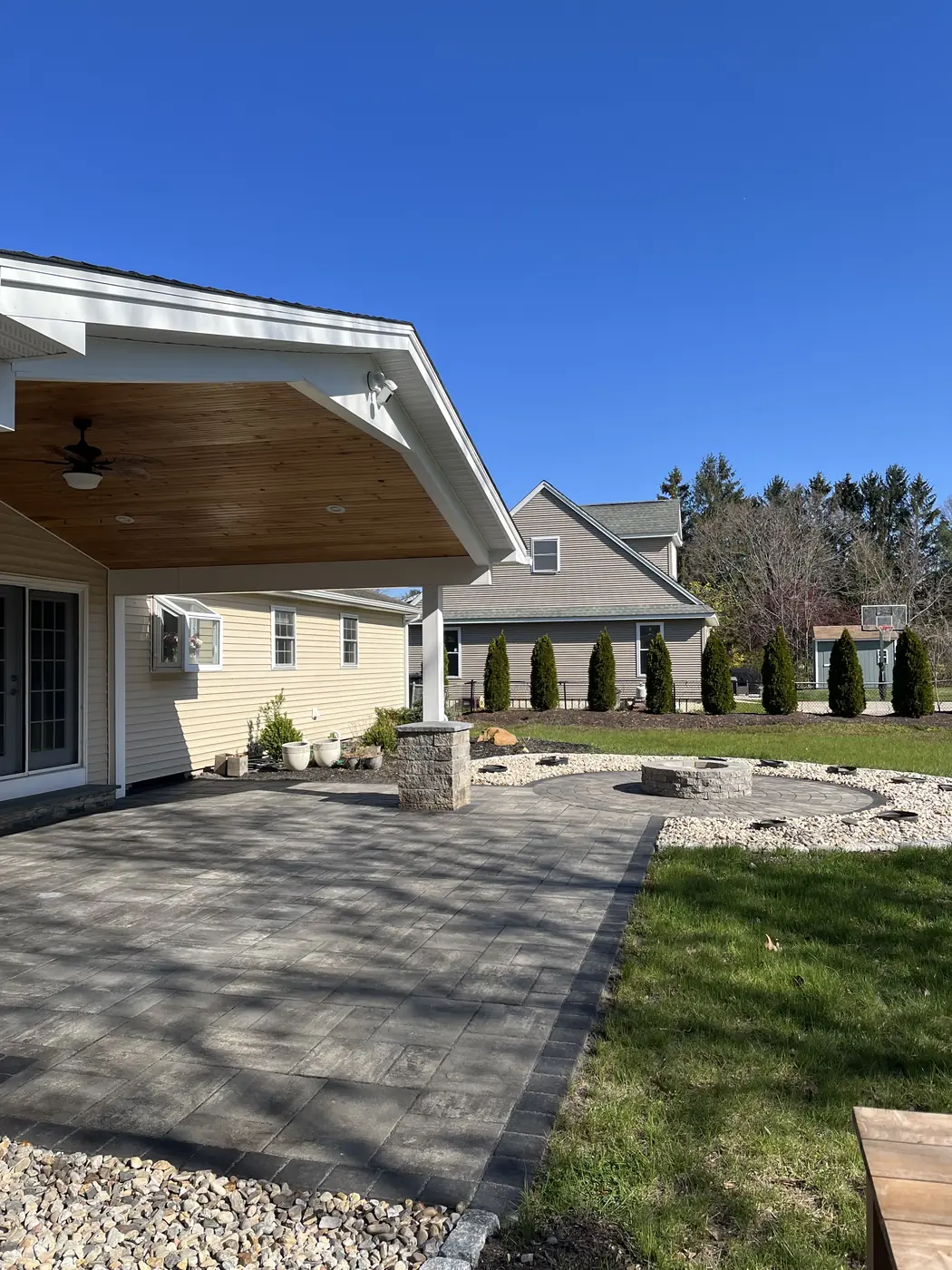 Covered porch patio, Southington Charcoal paver patio under a covered porch with a stone pillar and fire pit beyond in Southington, CT