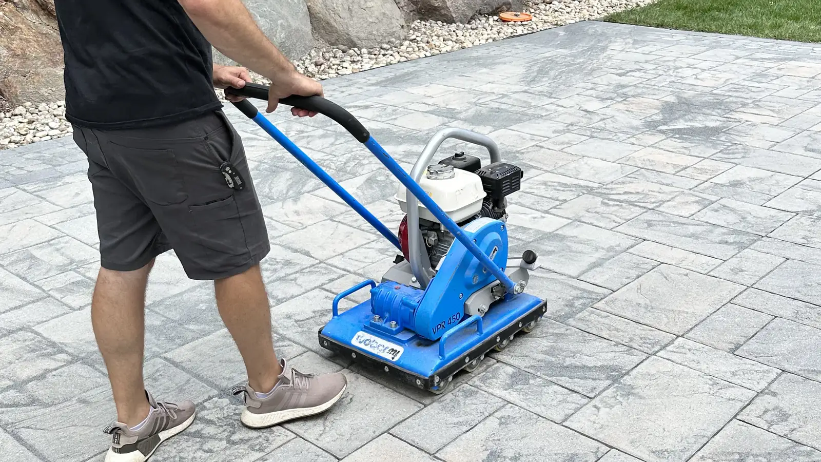 Locking in joint sand, Avon CleanScapes technician running a plate compactor over slab pavers to lock in joint sand in Avon, CT