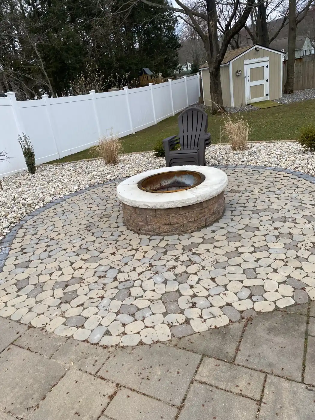 Stone fire pit on a circular cobble-pattern paver pad ringed with river rock in Southington, CT