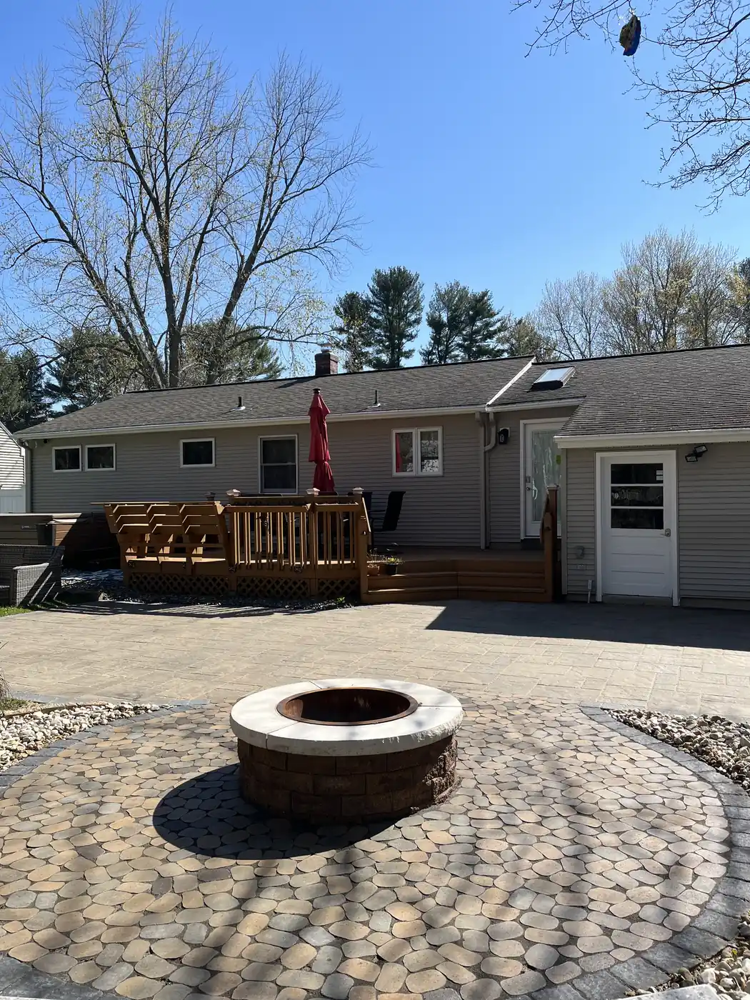Fire pit circle and deck Block fire pit on a circular cobble paver pad behind a ranch home with a wood deck in Southington, CT