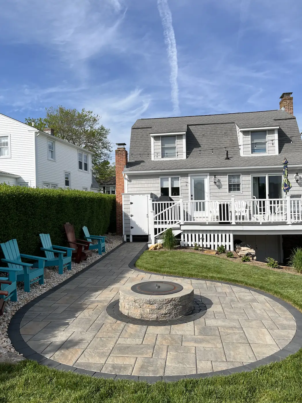 Paver patio with a round stone fire pit and charcoal border behind a cape home in Old Lyme, CT