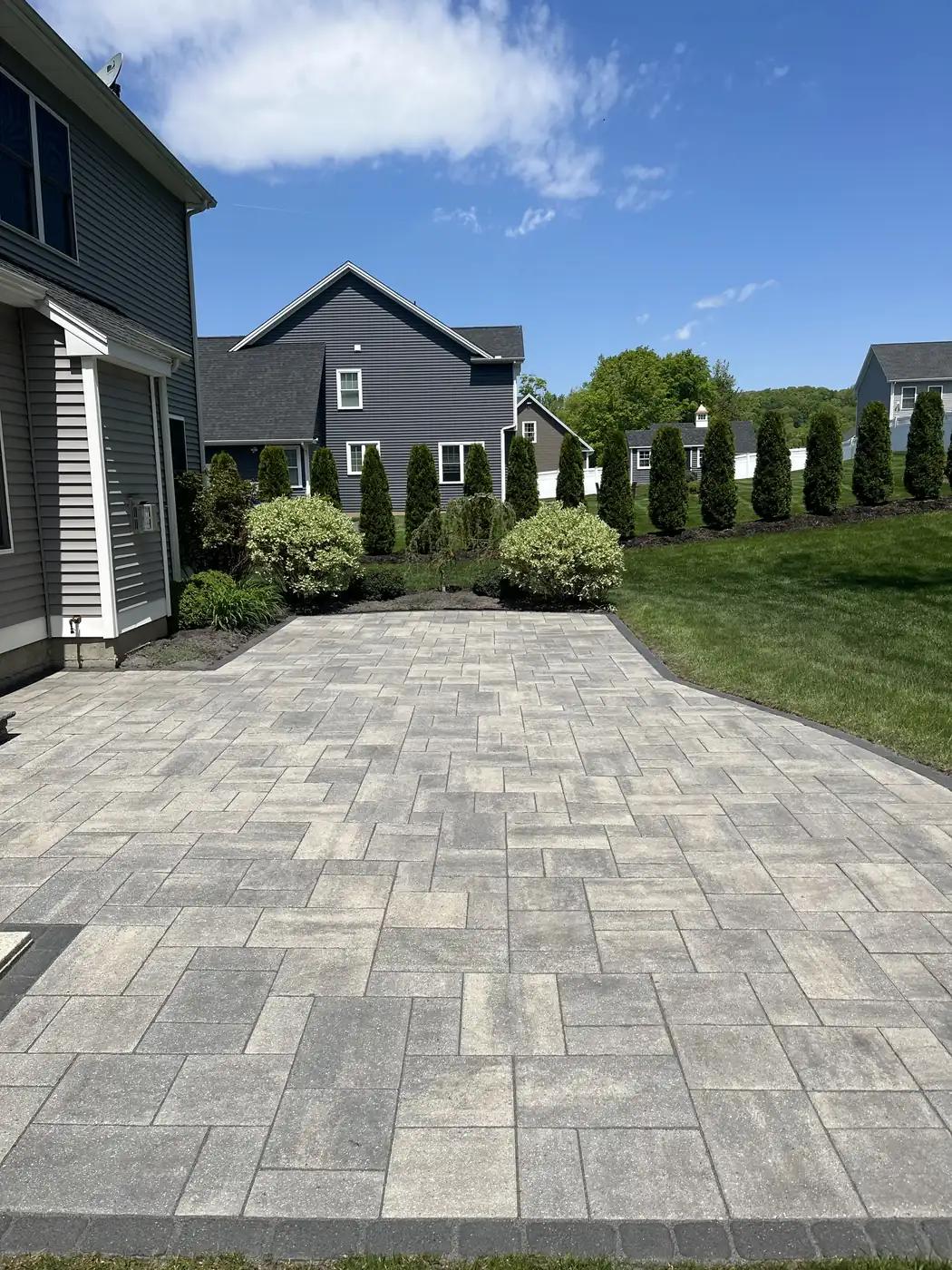 Cleaned gray paver patio edged in charcoal with an arborvitae hedge beyond in Southington, CT