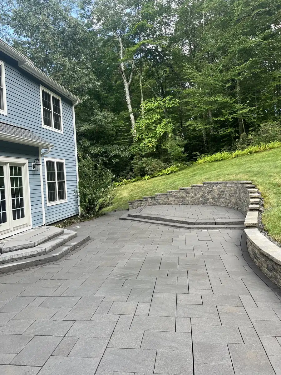 Patio and wall, Granby Gray paver patio with wide steps and a curved retaining wall behind a blue home in Granby, CT