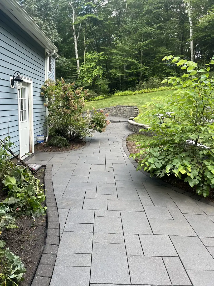Gray paver walkway with a border winding to stone steps beside a blue home in Granby, CT