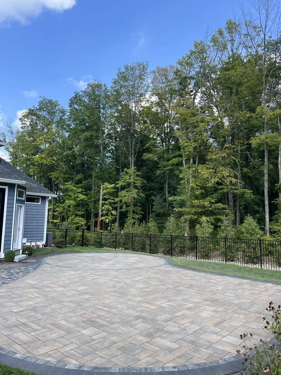 Kidney-shaped herringbone paver patio beside a black fence and woods in Southington, CT