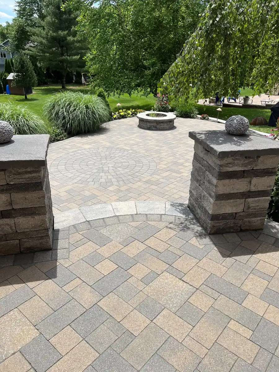 Paver patio entry between two stacked-stone pillars with a fire pit beyond in Rocky Hill, CT