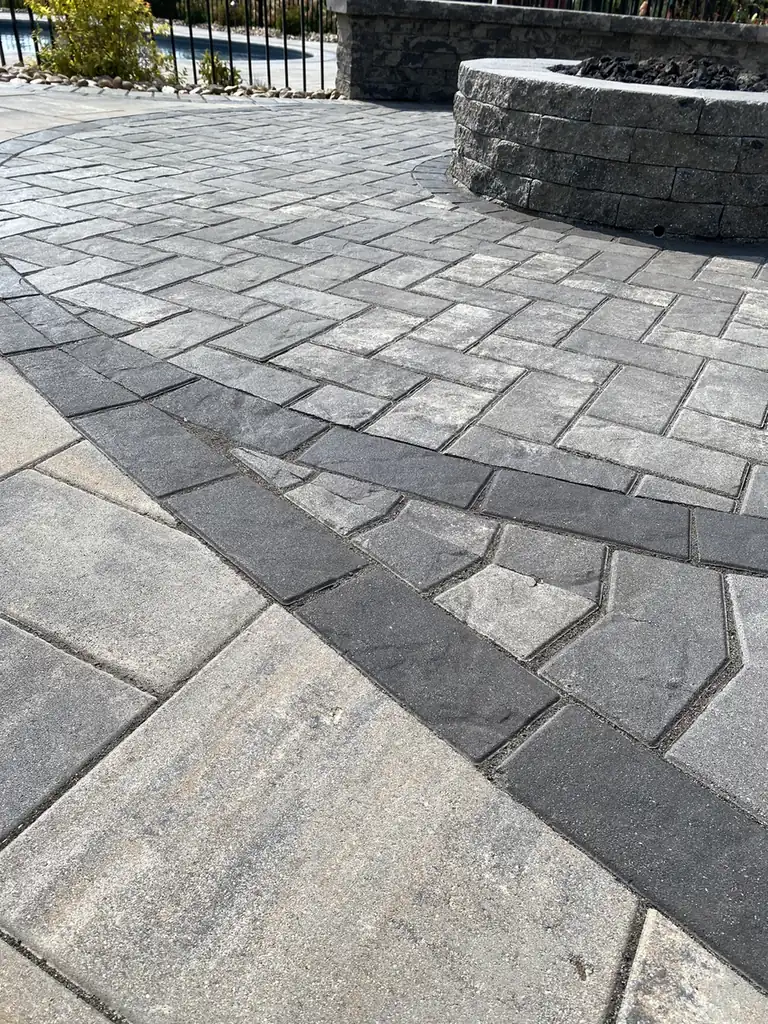Inlay band detail Close-up of gray pavers with a charcoal inlay band beside a block fire pit in Cromwell, CT