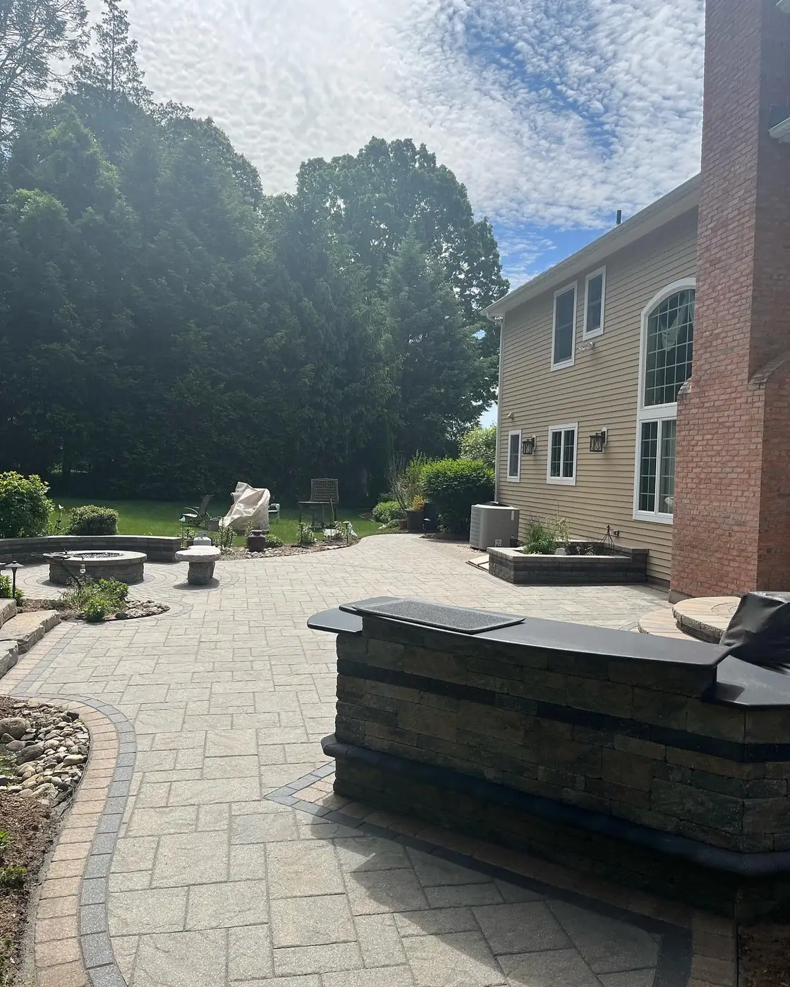 Paver patio with a stacked-stone bar counter beside a brick chimney in South Windsor, CT