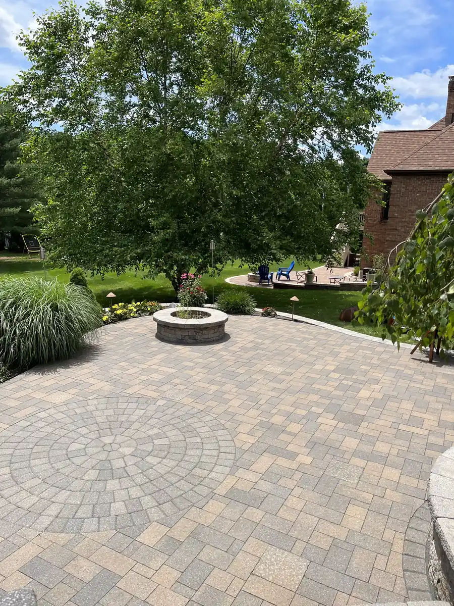 Paver patio with a circle inlay and stone fire pit under a shade tree in Rocky Hill, CT