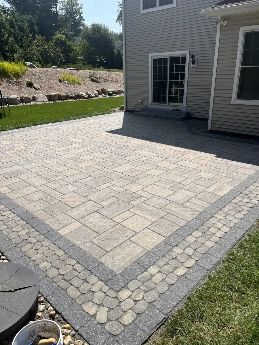 Paver patio with a cobble inlay band and gray border behind a home in Avon, CT