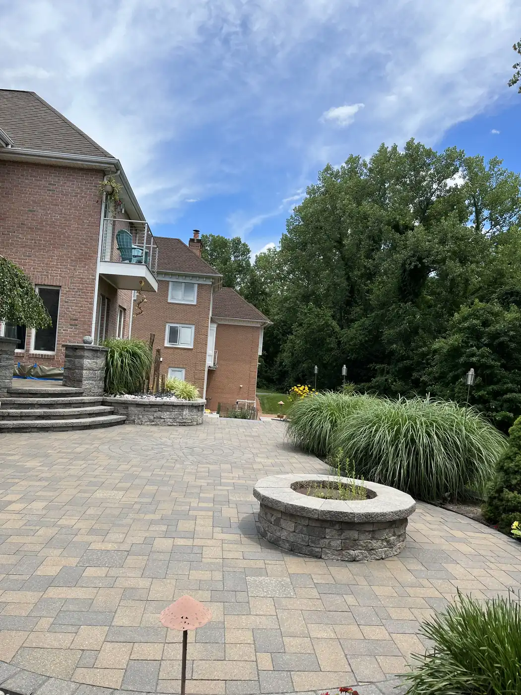 Paver patio with a block fire pit and ornamental grasses at a brick home in Rocky Hill, CT
