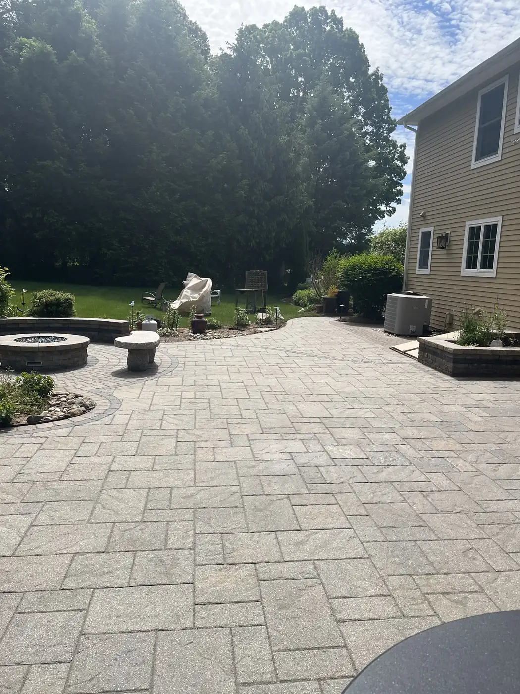 Wide paver patio with a fire pit, stone seat and planters after hardscape maintenance in South Windsor, CT