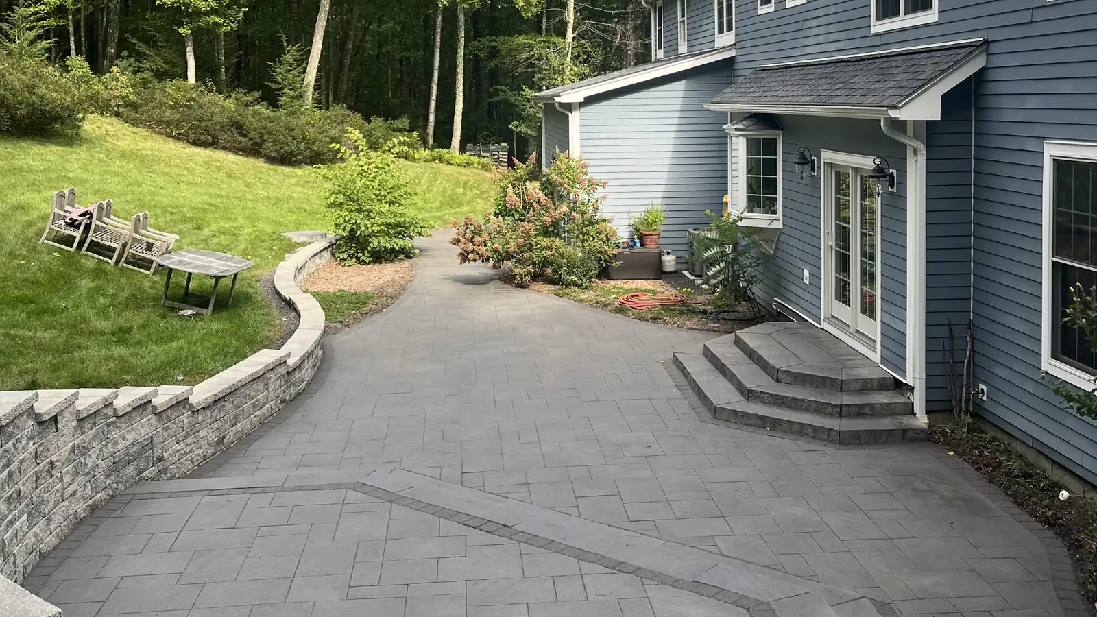 Patio overview, Granby Overview of a cleaned paver patio wrapped by a block retaining wall on a wooded lot in Granby, CT