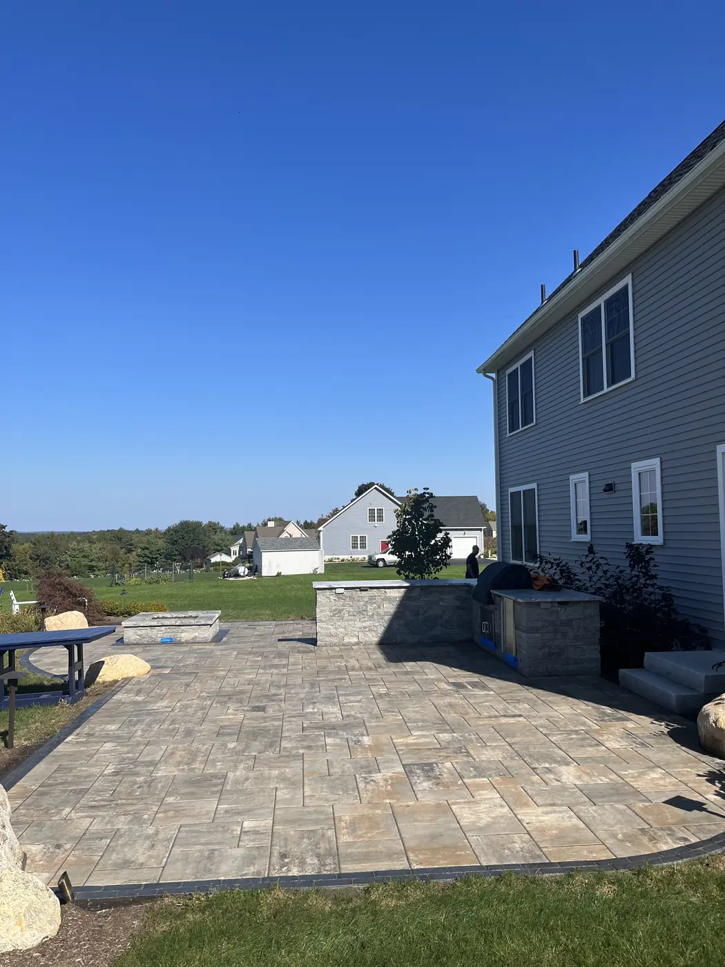 Paver patio with a dark border and stone bar behind a blue-gray home in Columbia, CT