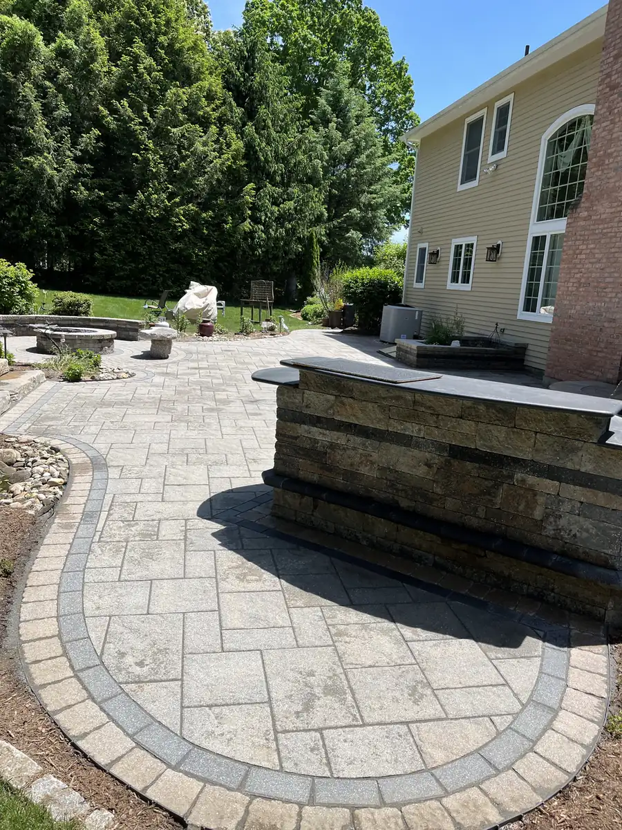 Paver patio with a curved border and a stone bar counter behind a home in South Windsor, CT