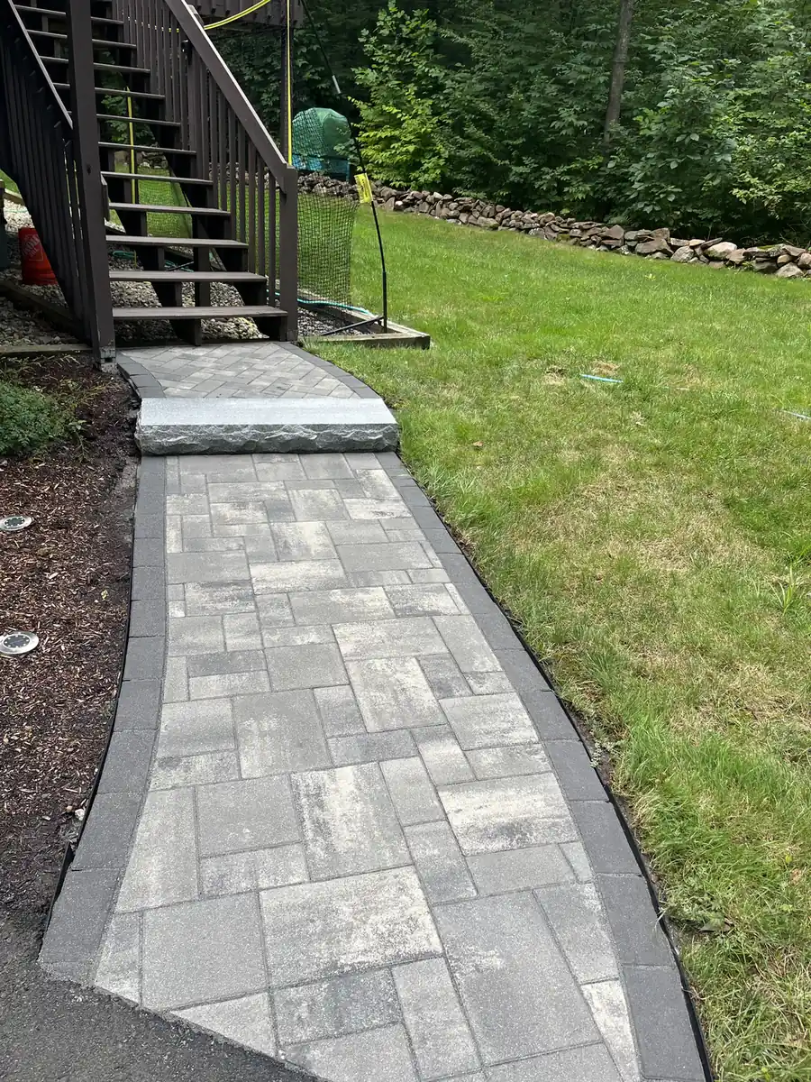 Paver walkway with a dark border ending at a granite step and deck stairs in Simsbury, CT