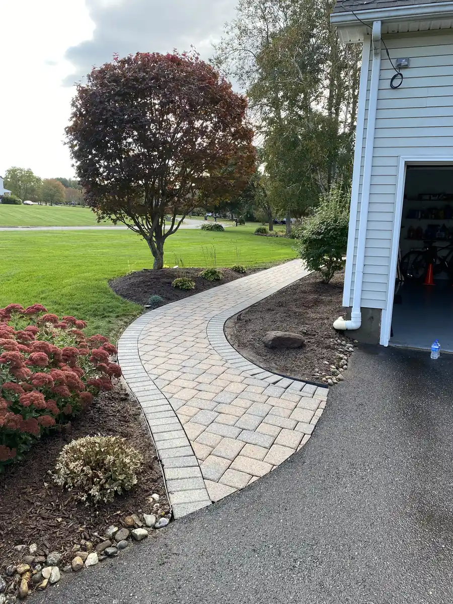 Curved paver walkway with a light border beside a garage and asphalt driveway in East Windsor, CT