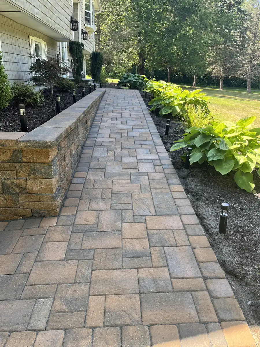 Long multi-tone paver walkway beside a low block retaining wall and hostas in Beacon Falls, CT