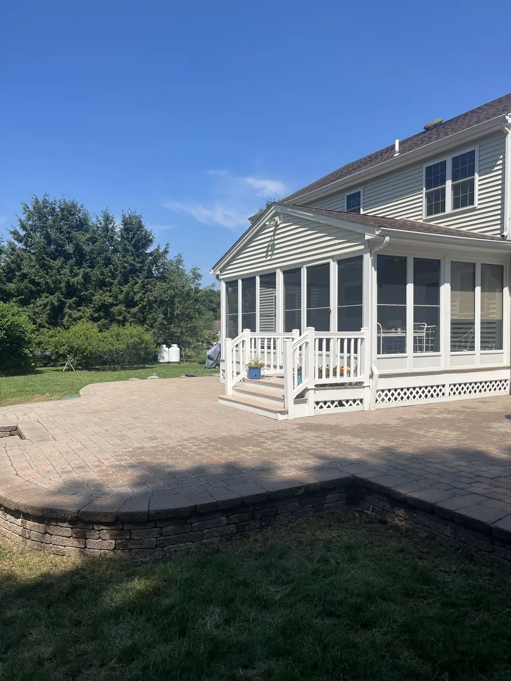 Raised paver patio on a block retaining wall beside a screened sunroom in Cheshire, CT