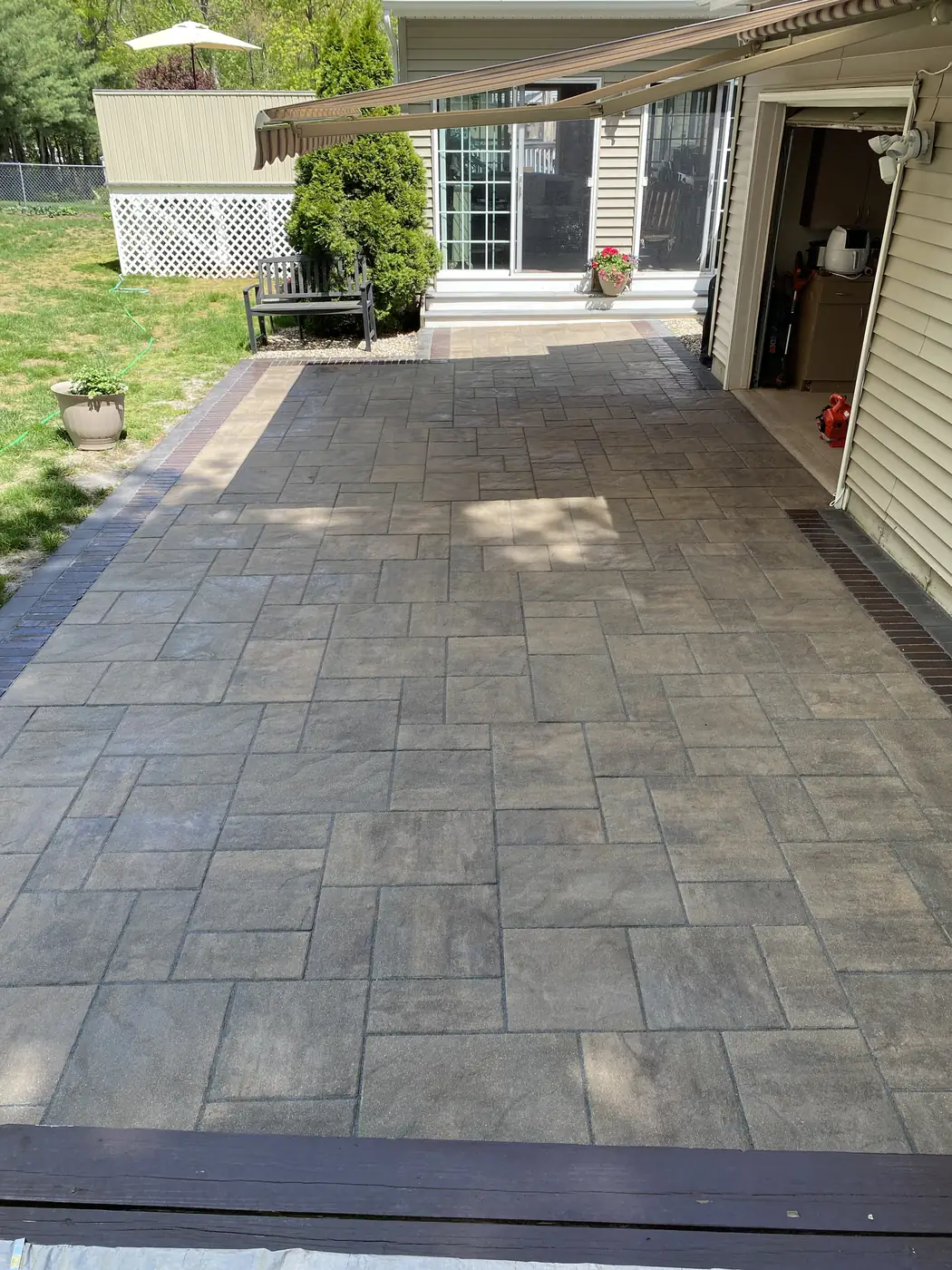 Slab patio, Bristol Large slab paver patio with a brick-red border under a retractable awning in Bristol, CT