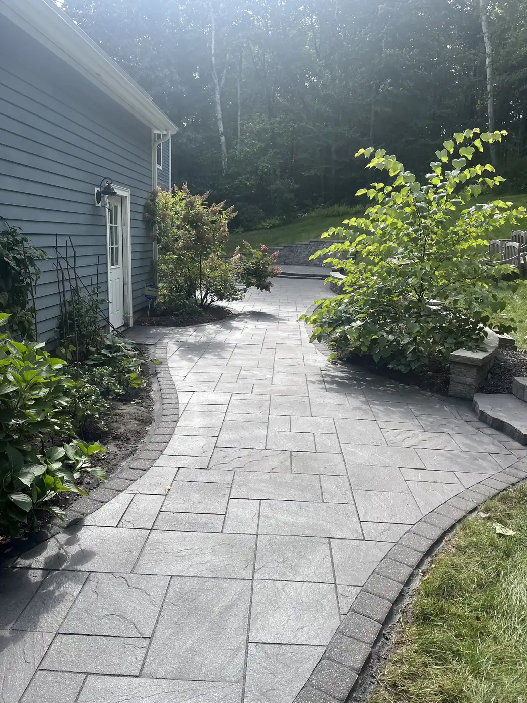 Slab paver walkway with a brown border curving along a woodland edge in Granby, CT