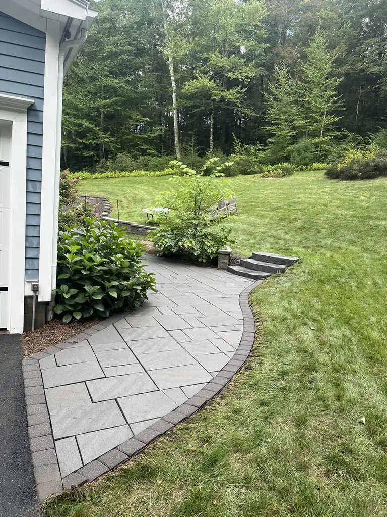Gray slab paver walkway with a brown border curving to stone steps in Granby, CT
