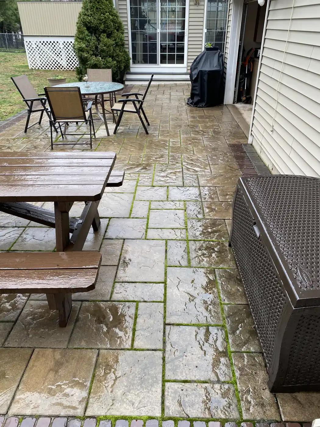 Stamped concrete wash, Bristol Stamped concrete patio mid-wash with moss still in the joints beside patio furniture in Bristol, CT