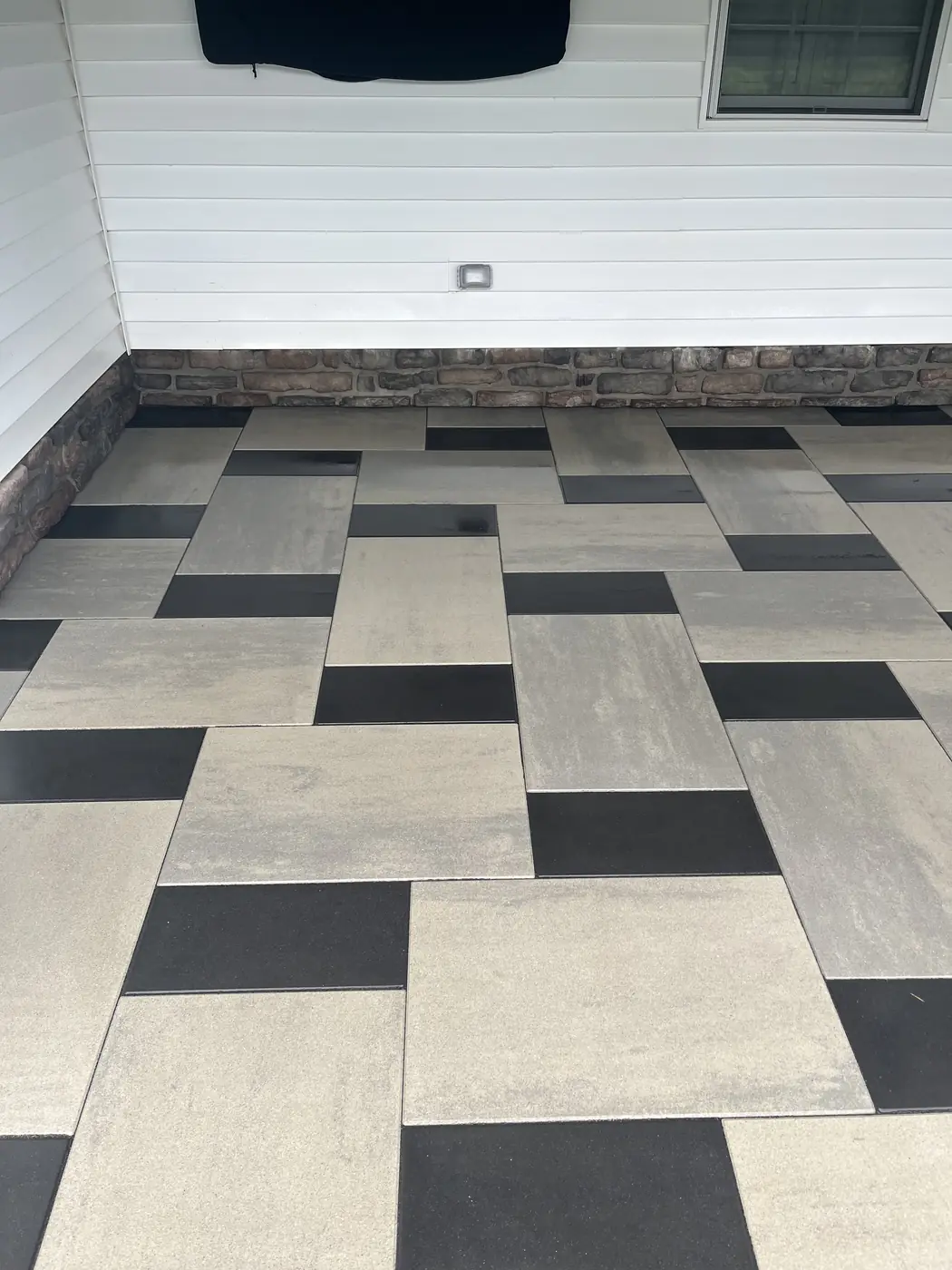 Two-tone slab patio, Glastonbury Two-tone gray and black slab patio cleaned along a stone-veneer house wall in Glastonbury, CT