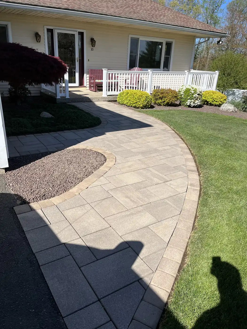 Wide tan slab paver walkway curving around a stone bed at a ranch home in Plainville, CT